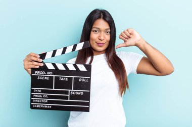 Genç Venezuelalı bir kadın mavi arka planda izole edilmiş bir klasör tutuyor gururlu ve kendinden emin hissediyor, örnek olarak.