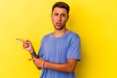 Sarı arka planda izole edilmiş beyaz dövmeli genç bir adam işaret parmağıyla fotokopi alanını işaret ederek heyecan ve arzusunu ifade ediyor..