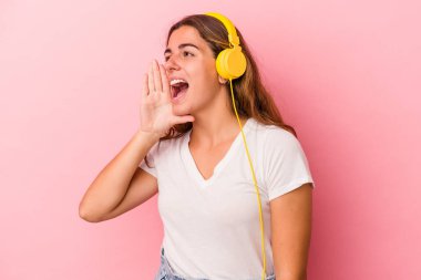 Pembe arka planda izole edilmiş müzik dinleyen beyaz bir kadın bağırıyor ve avuç içi kadar açık bir ağız tutuyor..