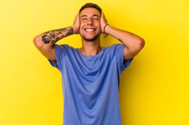 Sarı arka planda izole edilmiş dövmeleri olan beyaz bir genç ellerini başının üstünde tutarak gülüyor. Mutluluk kavramı.