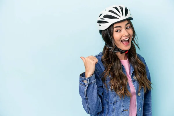 Young caucasian woman rinding a bike isolated on blue background points with thumb finger away, laughing and carefree.