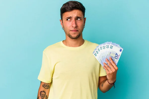 Hombre Caucásico Joven Sosteniendo Billetes Aislados Sobre Fondo Azul Confundido — Foto de Stock
