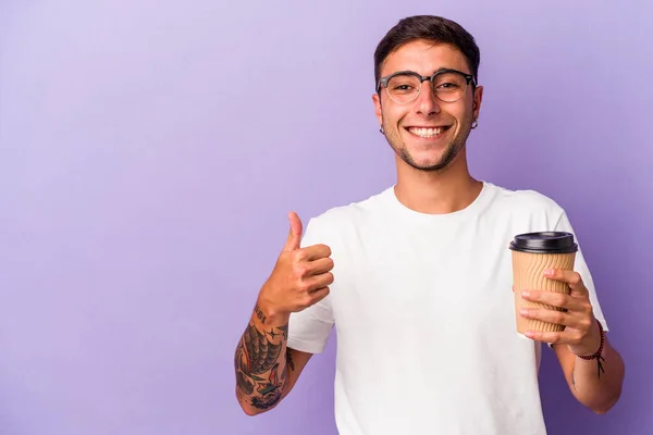 年轻的高加索人拿着咖啡 带着紫色背景的咖啡 微笑着举起大拇指 — 图库照片