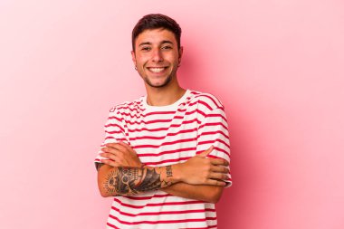 Sarı arka planda kendini güvende hisseden, kararlılıkla kollarını kavuşturan dövmeli beyaz bir genç..