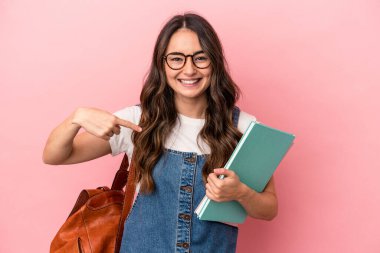 Young caucasian student woman isolated on pink background person pointing by hand to a shirt copy space, proud and confident