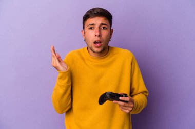 Genç beyaz adam elinde oyun kumandası tutuyor. Mor arka planda izole edilmiş. Şaşırmış ve şok olmuş..