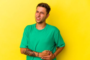 Sarı arka planda karaciğer ağrısı ve karın ağrısı olan dövmeli beyaz bir genç..