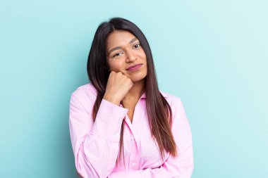 Genç Venezuelalı bir kadın mavi arka planda izole edilmiş, üzgün ve dalgın hisseden, kopyalama alanına bakan.