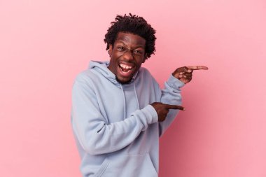 Pembe arka planda izole edilmiş genç Afro-Amerikalı adam işaret parmağıyla işaret ederek heyecanlanıyor..