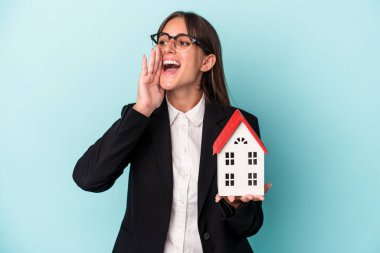 Mavi arka planda izole edilmiş oyuncak evi olan genç bir iş kadını avucunun içi gibi açık bir ağızla bağırıyor..