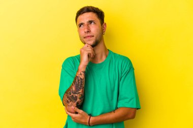 Sarı arka planda izole edilmiş dövmeleri olan genç, beyaz bir adam. Düşünüyor, düşünüyor, düşünüyor, hayal kuruyor..