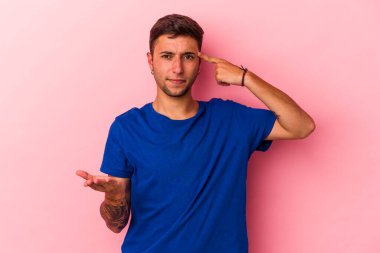 Sarı arka planda izole edilmiş dövmeleri olan genç beyaz bir adam elinde bir ürün taşıyor..