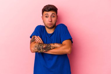 Sarı arka planda izole edilmiş dövmeleri olan beyaz genç bir adam omuzlarını silker ve gözleri açık kalır..