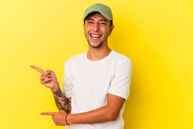 Sarı arka planda izole edilmiş beyaz dövmeli genç bir adam işaret parmağıyla fotokopi alanını işaret ederek heyecan ve arzusunu ifade ediyor..