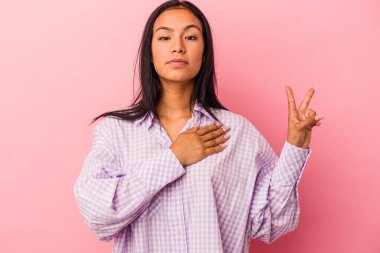 Pembe arka planda izole edilmiş genç Latin kadın yemin ediyor, elini göğsüne koyuyor..