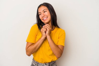 Beyaz arka planda izole edilmiş genç Latin bir kadın şans için dua ediyor, şaşırmış ve ağzını açıp önüne bakıyor..