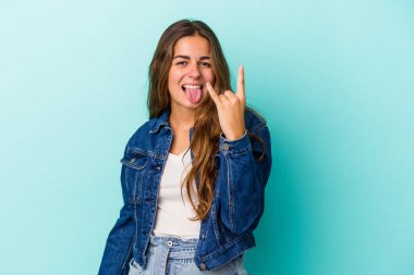 Mavi arka planda izole edilmiş genç beyaz kadın parmaklarıyla taş hareketi gösteriyor.