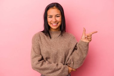 Pembe arka planda izole edilmiş genç Latin kadın işaret parmağıyla işaret ederek gülümsüyor..