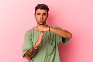 Sarı arka planda izole edilmiş dövmeleri olan genç beyaz bir adam, bir zaman aşımı hareketi gösteriyor..