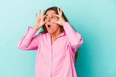 Mavi arka planda izole edilmiş genç beyaz kadın bir başarı fırsatı bulmak için gözlerini açık tutuyor..