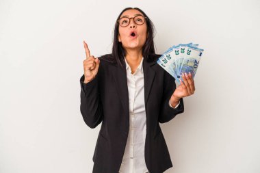 Elinde banknotlar tutan genç Latin kadın beyaz arka planda izole edilmiş kahve ağzı açık, üst tarafı işaret ediyor..