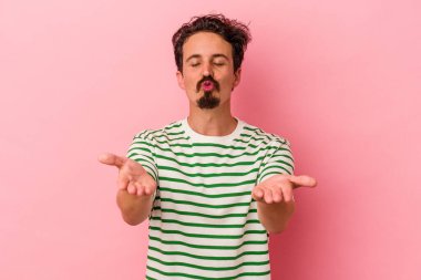 Genç beyaz adam pembe arka planda izole edilmiş dudaklar kıvrılmış ve hava öpücüğü göndermek için avuç içleri tutulmuş..