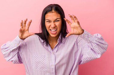 Pembe arka planda izole edilmiş genç Latin kadın pençelerini kedi taklidi yaparken gösteriyor, agresif bir hareket..