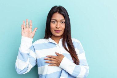 Genç Venezuelalı bir kadın mavi arka planda izole edilmiş yemin ediyor, elini göğsüne koyuyor..