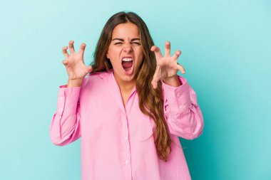 Mavi arka planda izole edilmiş genç beyaz kadın gergin elleriyle çığlık atıyor..