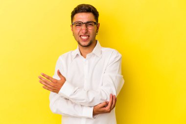 Dövmeleri olan beyaz bir genç adam sarı arka planda izole edilmiş dirsek masajı yapıyor, kötü bir hareketin ardından acı çekiyor..