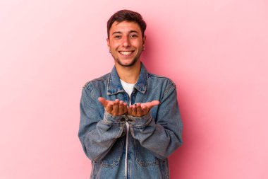 Sarı arka planda izole edilmiş beyaz dövmeli genç bir adam avuçlarıyla bir şey tutuyor ve kameraya sunuyor..