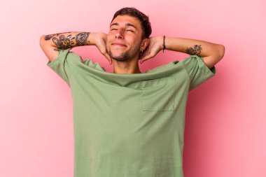 Sarı arka planda izole edilmiş, elleri başının arkasında kendinden emin dövmeleri olan genç, beyaz bir adam..