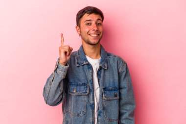 Sarı arka planda dövmeleri olan genç beyaz bir adam bir numarayı parmağıyla gösteriyor..