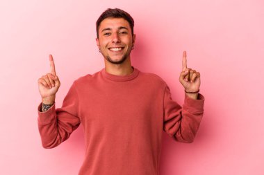 Sarı arka planda dövmeleri olan beyaz genç bir adam iki ön parmağı da boş bir alan gösteriyor..