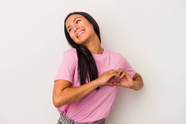 Beyaz arka planda izole edilmiş genç Latin kadın gülümsüyor ve elleriyle kalp şekli gösteriyor..