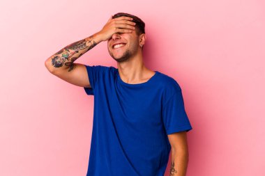 Sarı arka planda izole edilmiş dövmeleri olan genç, beyaz bir adam. Gözleri ellerle kaplıyor. Gülümsüyor ve bir sürpriz bekliyor..