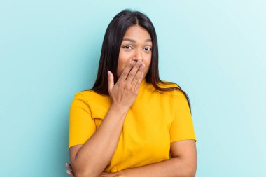 Genç Venezüellalı bir kadın mavi arka planda izole edilmiş esniyor. Ağzı eliyle kapatan yorgun bir hareket sergiliyor..