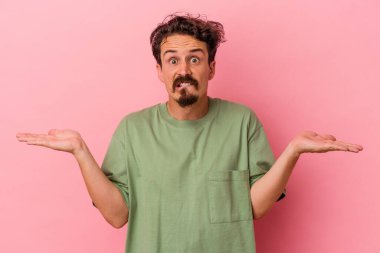 Kafkasyalı genç adam pembe arka planda izole edilmiş. Kafası karışmış ve omuz silkiyor. Kopya alanını tutmak için..