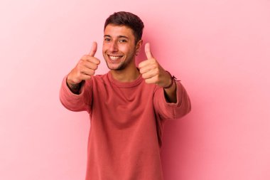 Sarı arka planda izole edilmiş beyaz dövmeli genç bir adam. Baş parmağını kaldırıyor, gülümsüyor ve kendinden emin..