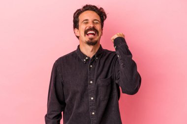 Pembe arka planda izole edilmiş genç beyaz bir adam zaferi, tutkuyu ve coşkuyu kutluyor, mutlu bir ifade..