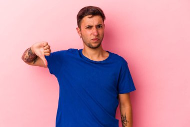 Sarı arka planda izole edilmiş beyaz dövmeli genç bir adam baş parmağını aşağı gösteriyor, hayal kırıklığı konsepti..