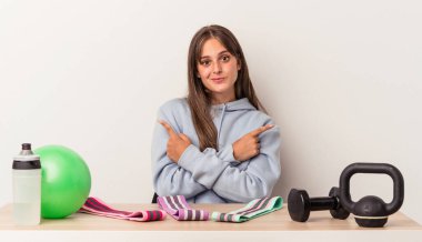 Beyaz arka plan noktalarına izole edilmiş spor ekipmanlarıyla masada oturan beyaz bir kadın iki seçenek arasında seçim yapmaya çalışıyor..