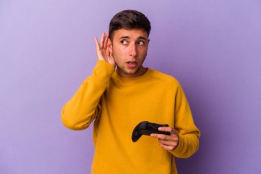 Kafkasyalı genç bir adam oyun kontrolörünü mor arka planda izole edip bir dedikoduyu dinlemeye çalışıyor..