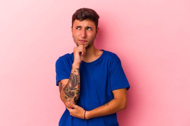 Sarı arka planda izole edilmiş, şüpheli ve şüpheci bir ifadeyle yan bakan beyaz dövmeli genç bir adam..