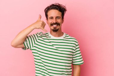Pembe arka planda izole edilmiş genç beyaz adam parmaklarıyla bir cep telefonu hareketi gösteriyor..