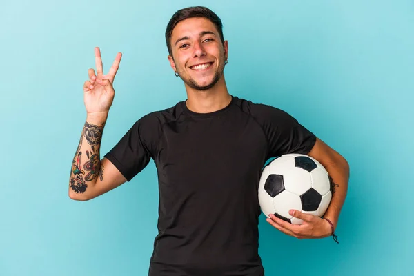 Młody Człowiek Gra Piłkę Nożną Trzymając Piłkę Niebieskim Tle Radosny — Zdjęcie stockowe