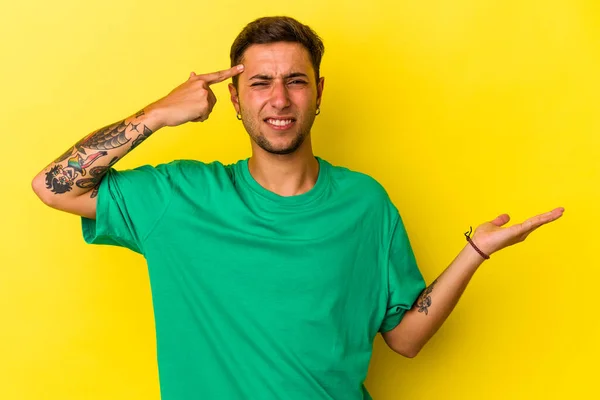 Young Caucasian Man Tattoos Isolated Yellow Background Holding Showing Product —  Fotos de Stock