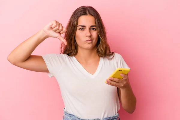 年轻的高加索女人用被粉色背景隔离的手机表现出不喜欢的手势 低垂大拇指 不同意的概念 — 图库照片