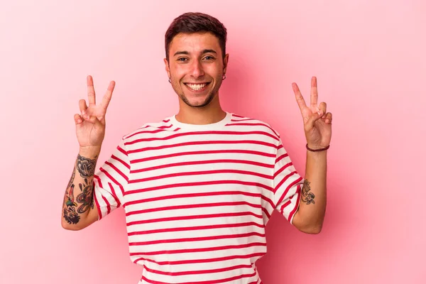 Sarı arka planda izole edilmiş dövmeleri olan genç beyaz adam zafer işareti gösteriyor ve gülümsüyor..