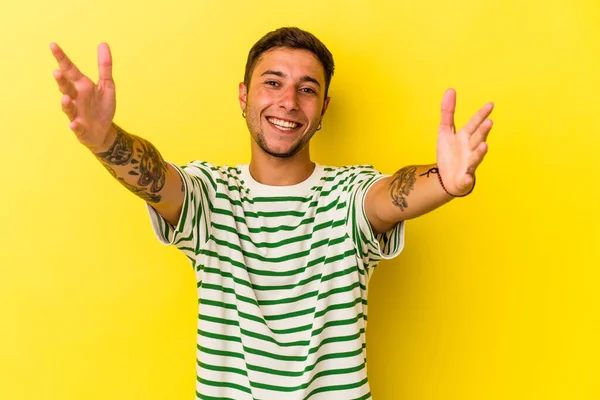 Sarı arka planda dövmeleri olan beyaz bir adam kameraya sarıldığı için kendini güvende hissediyor..